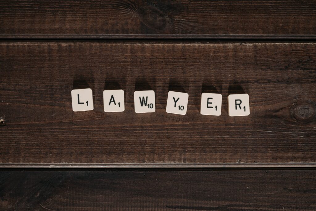 Scrabble tiles on a dark wood desk depicting the word "Lawyer"